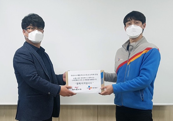 ▲NS홈쇼핑 물류센터 박민욱 팀장(왼쪽)이 CJ대한통운 관계자에게 마스크와 손소독제를 전달한 후 기념촬영을 하고 있다.