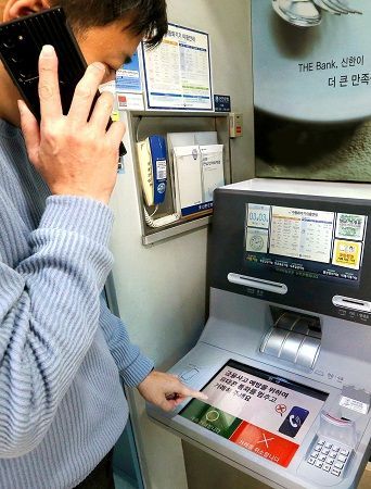 ▲ 고객이 핸드폰으로 통화하며 신한은행 ‘AI이상행동탐지ATM’을 이용하고 있는 도중 ATM 화면에 금융사고 예방 주의 문구가 나오고 있다.
